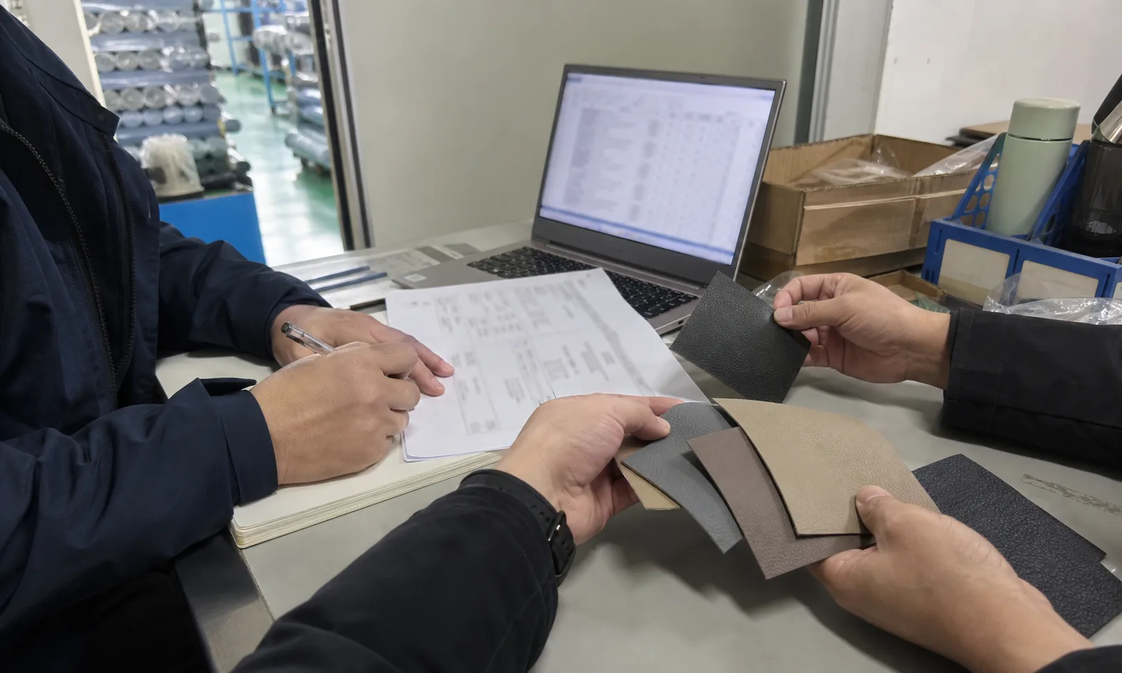 工作人员在工厂资料桌旁记录人造革样品用途并核对电脑和报价资料