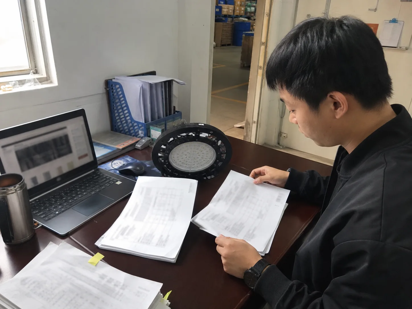 外贸人员在工厂办公室桌边对照光源样件和两份报价资料