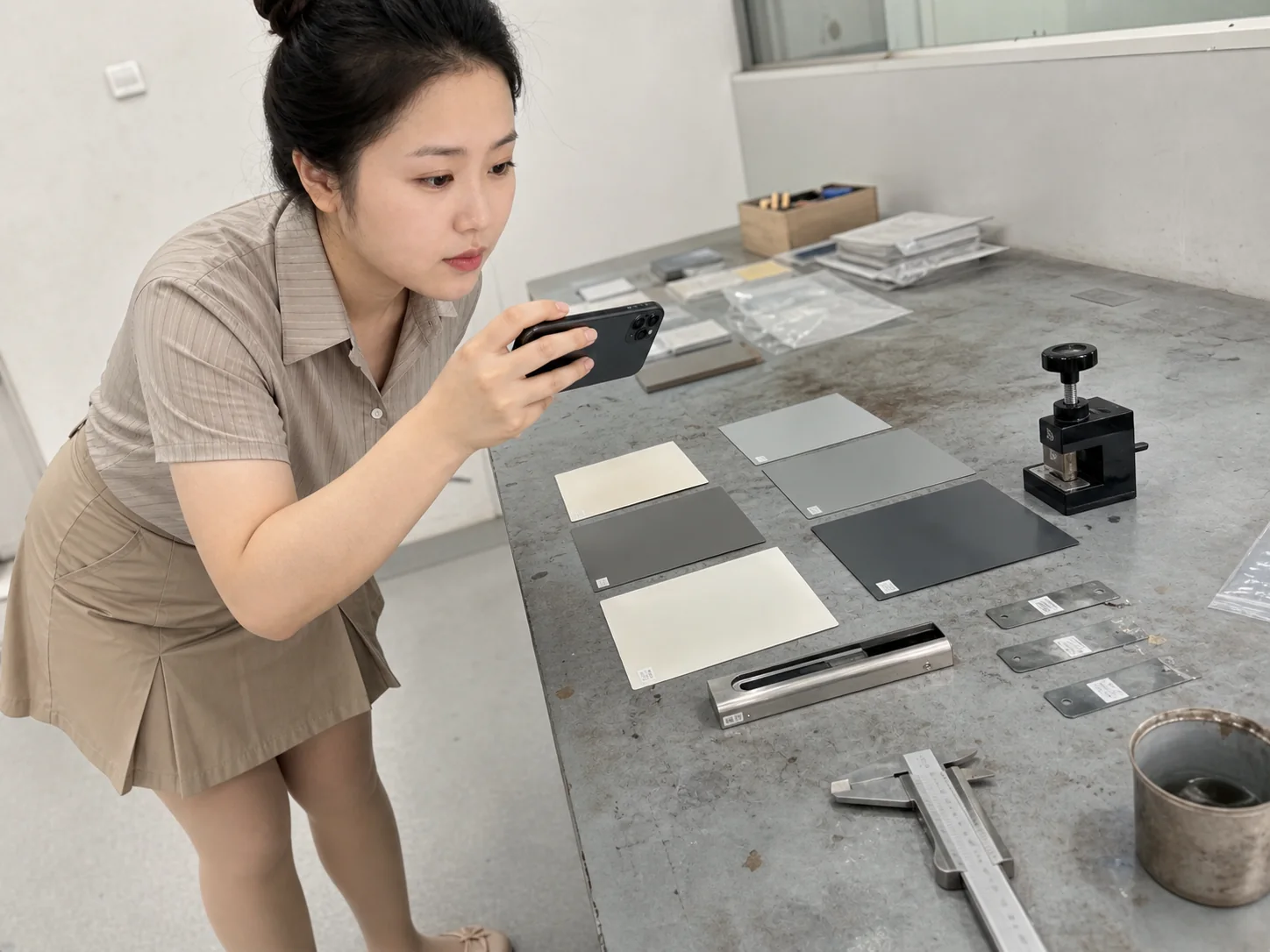 女性自媒体拍摄人员在金属涂装试样台用手机记录涂层样板、底材和附着力工具